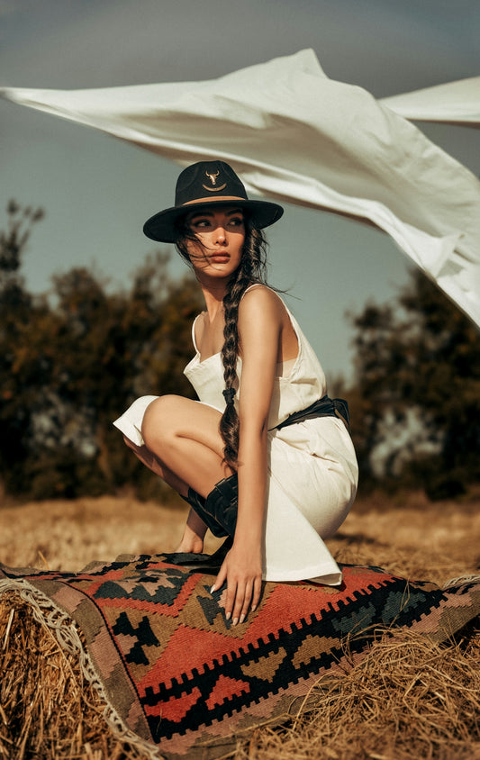 Woman in hat and white dress on rug in field