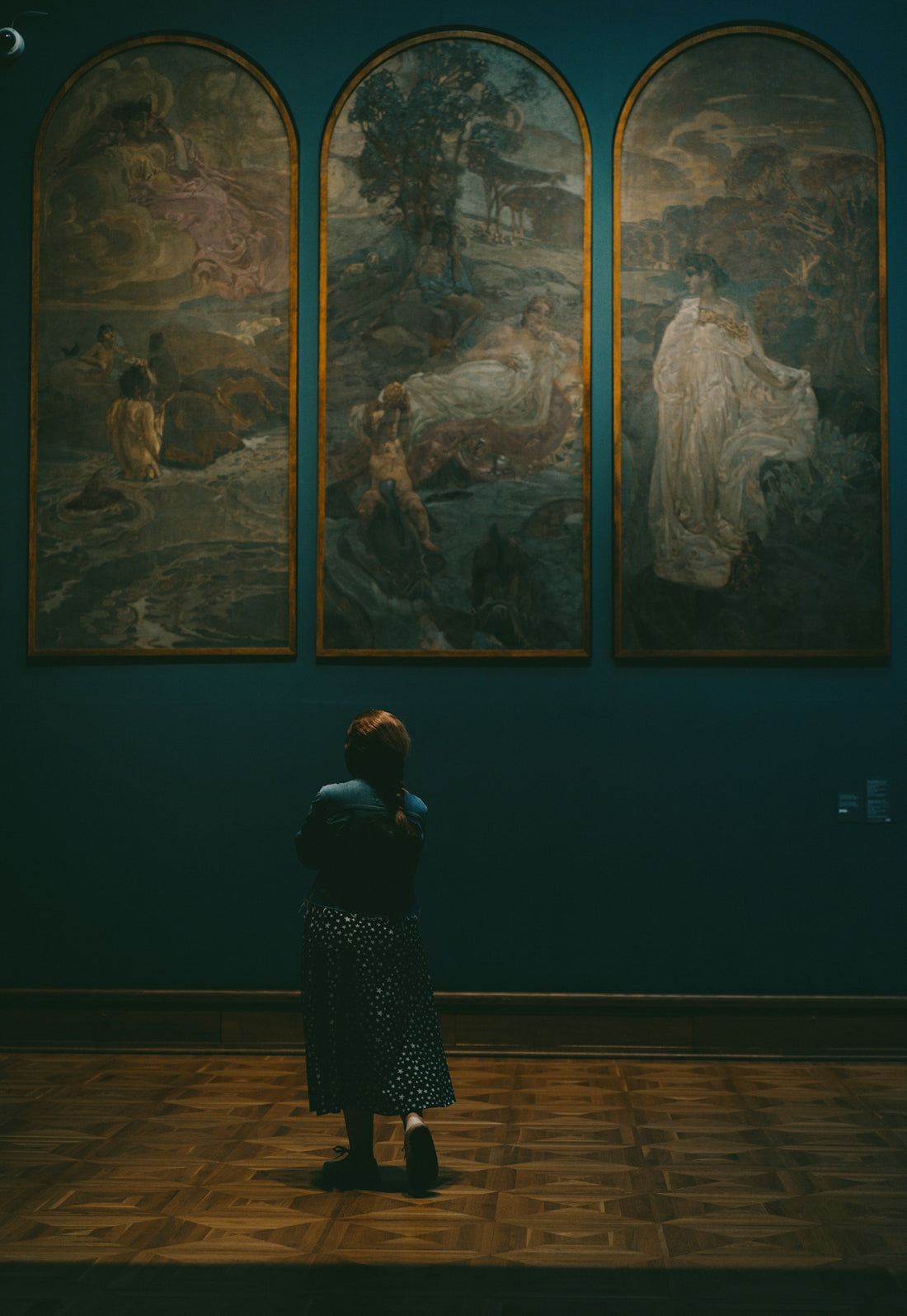 Woman observing three arched paintings in a museum