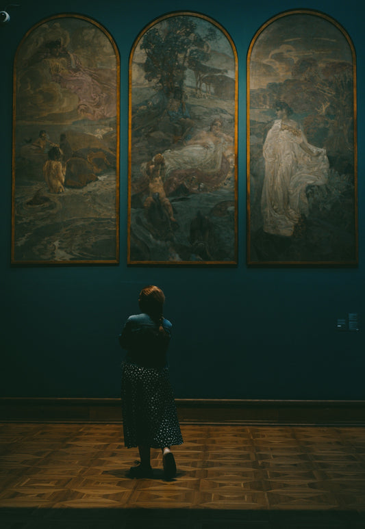 Woman observing three arched paintings in a museum