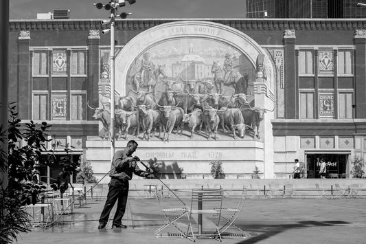 Man watering plants in front of a building with mural