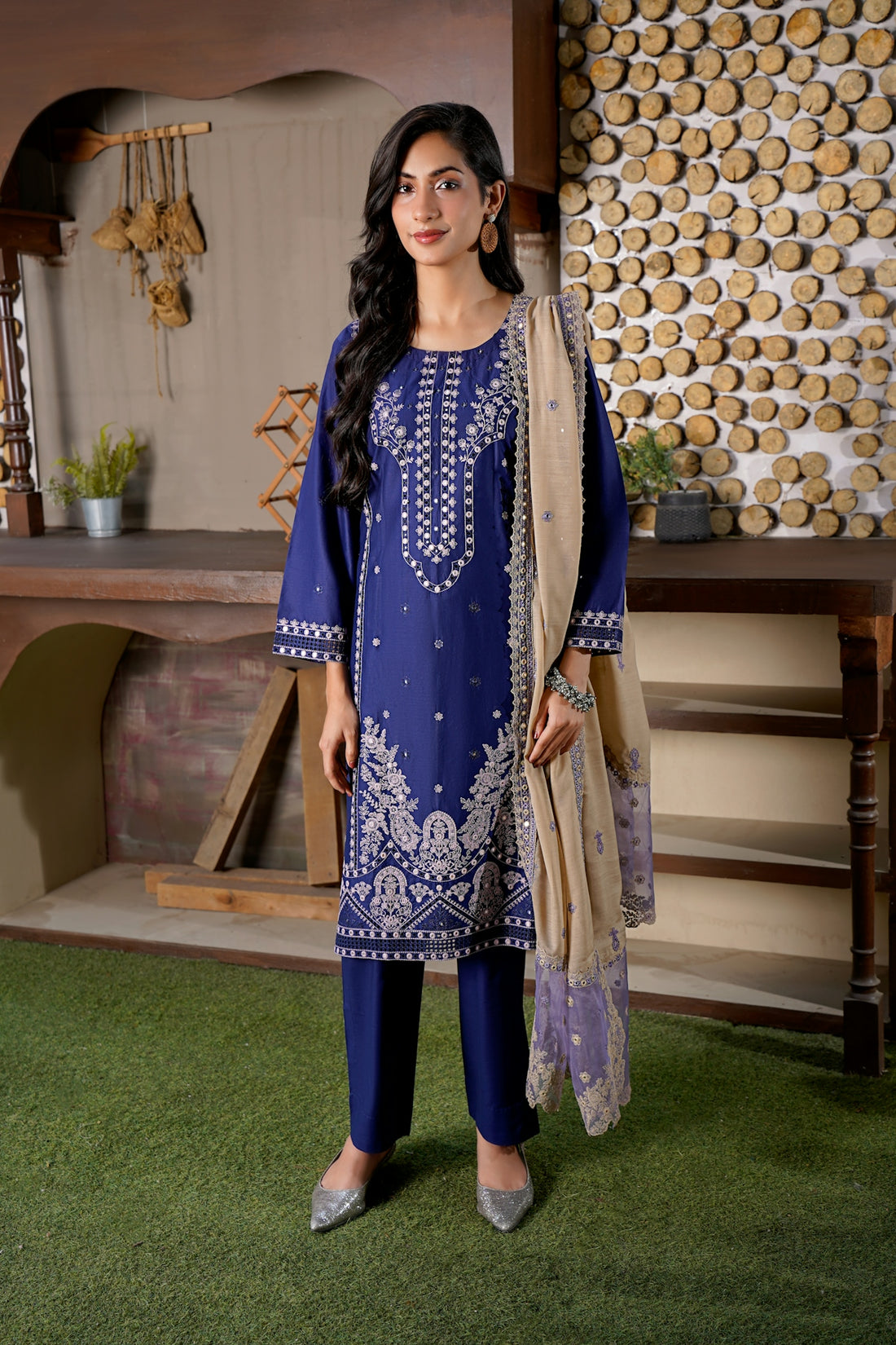 Woman in a blue embroidered outfit with a beige scarf.