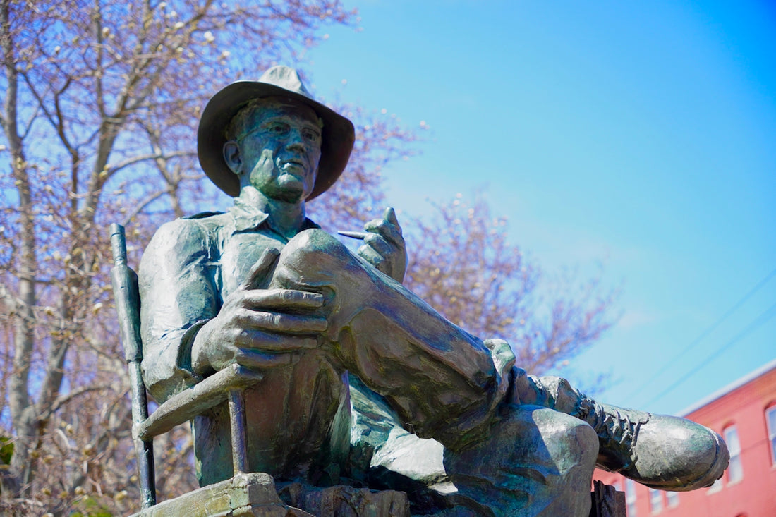 Bronze statue of a man sitting in a chair outdoors.