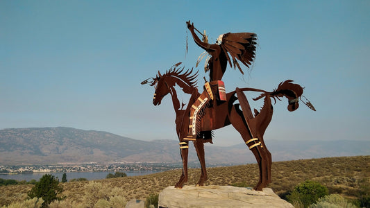 Native american metal sculpture on horseback overlooking a scenic landscape.