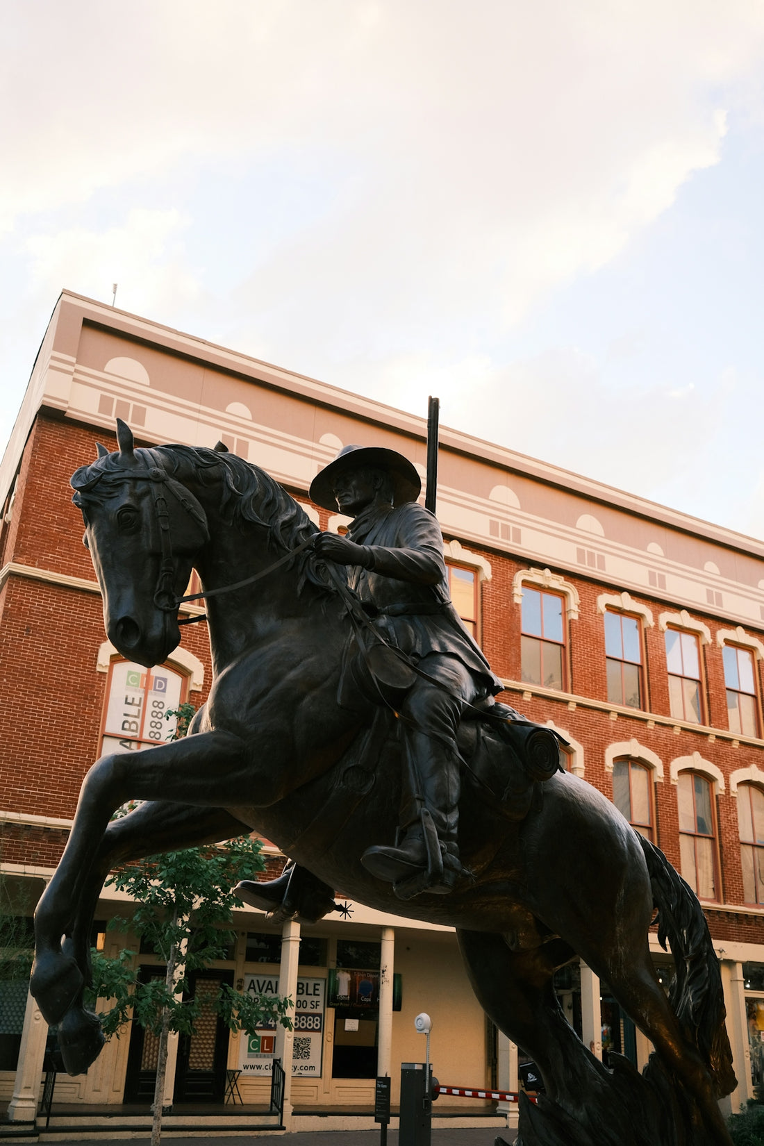 Bronze cowboy statue on rearing horse before a brick building.