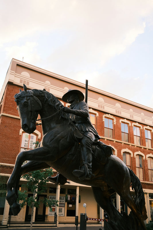 Bronze cowboy statue on rearing horse before a brick building.